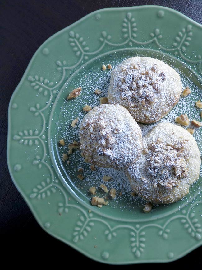 3 baked Date Thumbprint Cookies with Walnuts (Koloocheh) on green plate with powdered sugar, ready for serving.