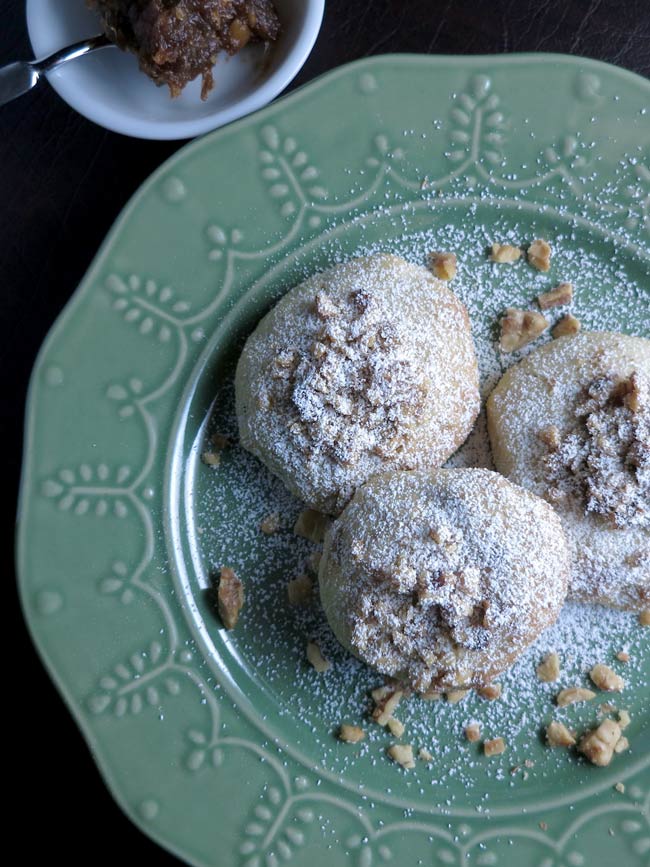 3 Date Thumbprint Cookies with Walnuts (Koloocheh) on green plate with powdered sugar sprinkled over all.