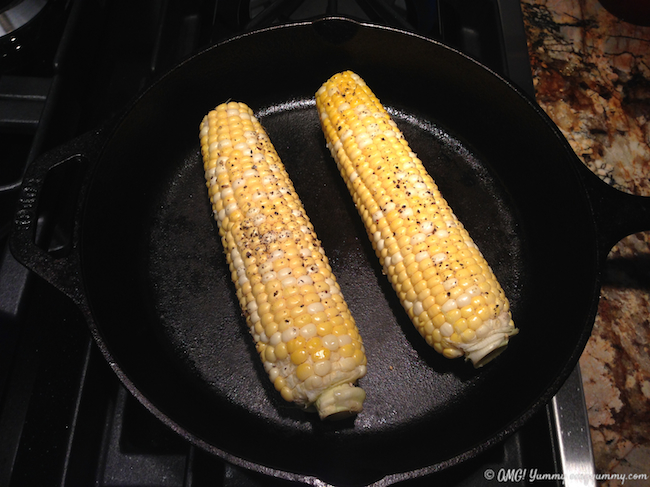 Cast iron pan with corn on the cob cooking on the hot surface.
