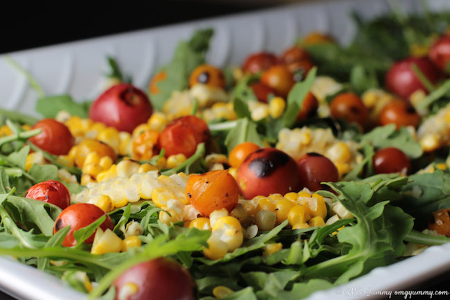 Blistered tomatoes,  fresh corn off the cob tossed with arugula in a white serving platter.