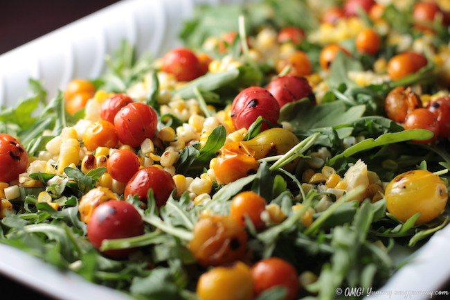 Tomato, Corn, and Arugula Salad tossed together in a white platter.