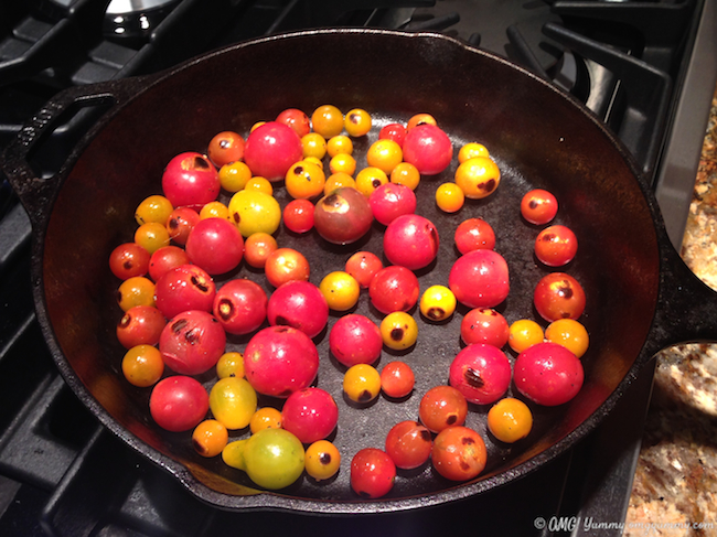 Multi-colored cherry tomatoes blistering in a hot cast iron frying pan.