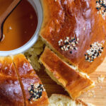 A pinterest image showing the round challah with slice cut out of it and honey in the middle.