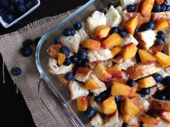 Challah bread pudding with peaches and blueberries in a glass baking dish ready for the oven.