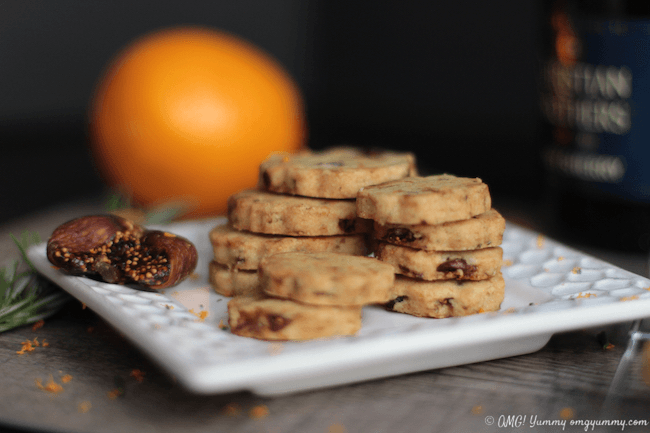 A platter of Fig Cocktail Cookies stacked up on a white platter with fig garnish and a whole orange.