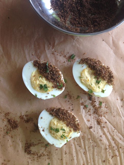 Deviled eggs with a line of dukkah sprinkled down one side of each egg on parchment paper.