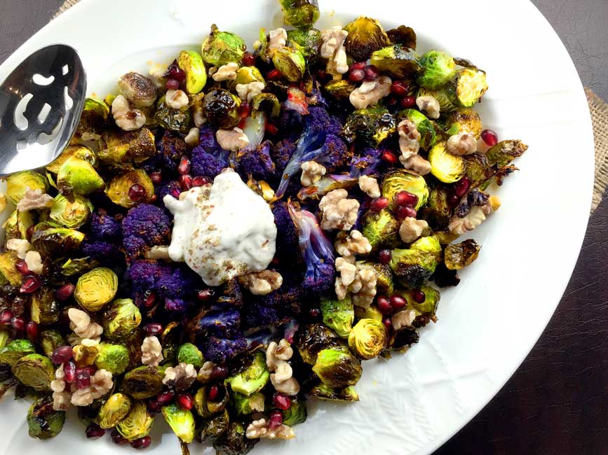 Roasted brussels sprouts on white plate with serving spoon.