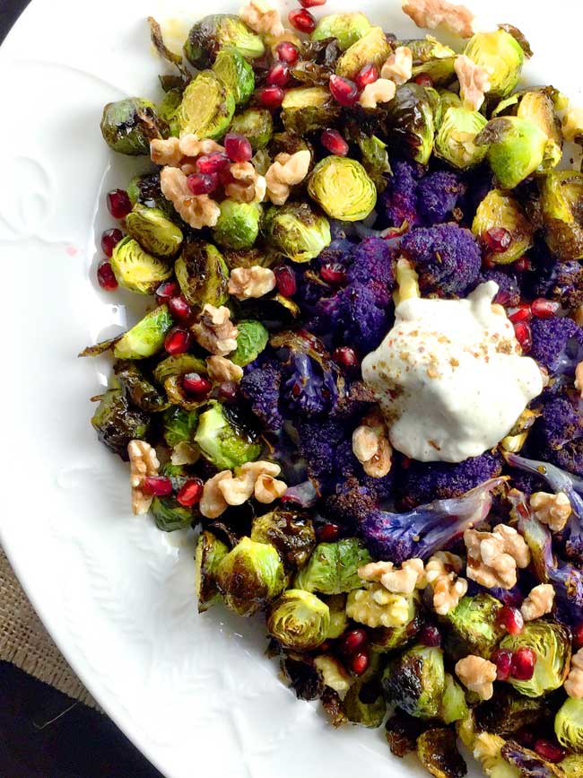 Roasted brussels sprouts and purple cauliflower with yogurt topping on a white platter ready for serving.