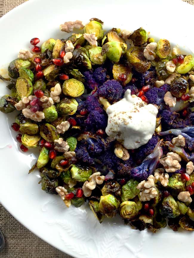 Brussels sprouts and cauliflower on a white plate with yogurt topping.
