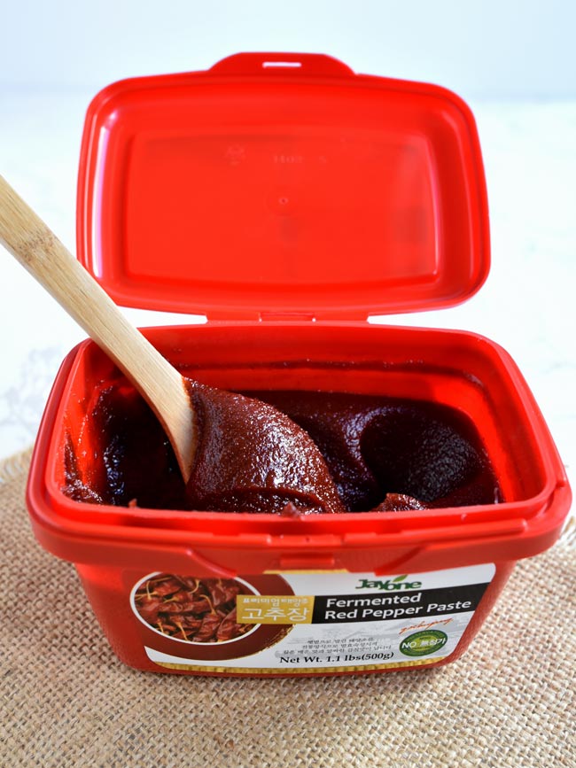 Gochujang fermented red pepper spice paste in red container with a wooden spoon.
