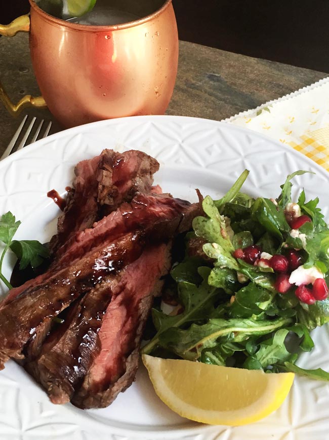 Flank steak on white plate with salad and copper mug