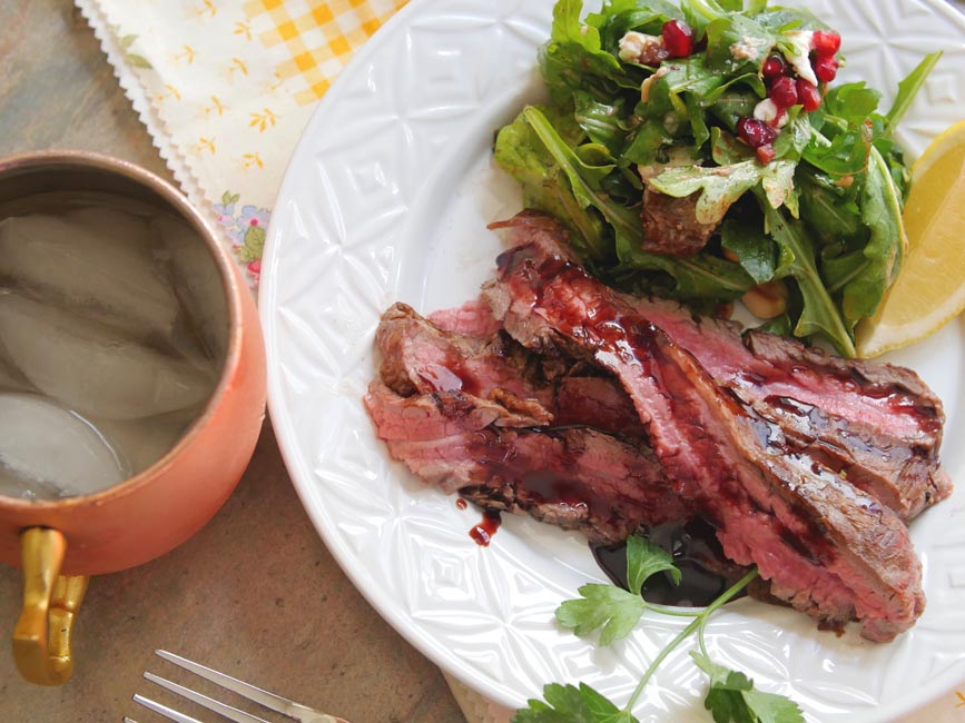 flank steak with pomegranate molasses on white plate with arugula salad