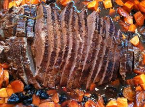 brisket in large pan with gravy and vegetables surrounding it