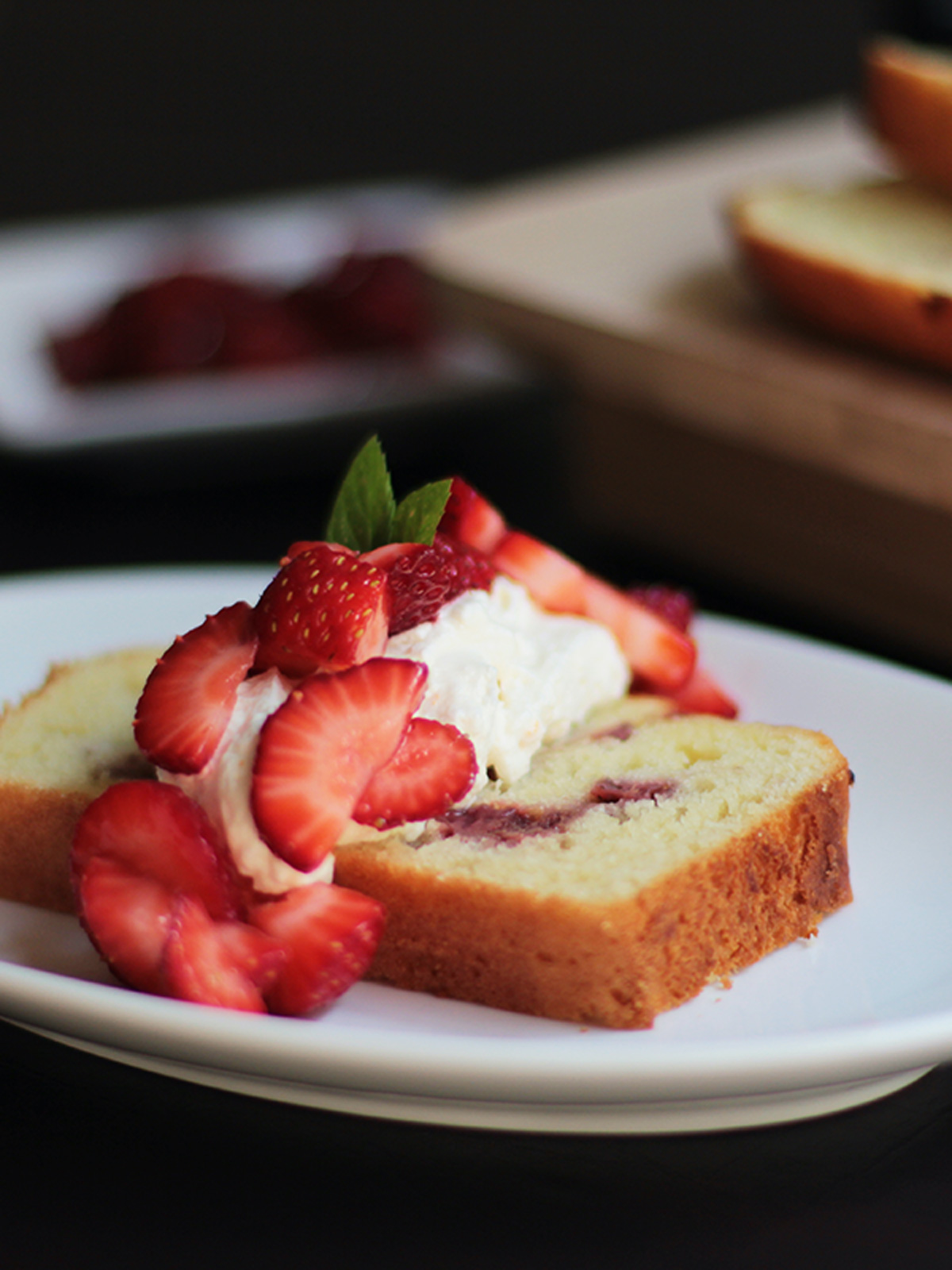 Strawberry shortcake loaf slice on white plate with the whole loaf and extra roasted strawberries in the background.
