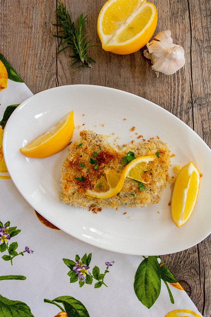 A serving of breaded lemon garlic chicken on a white plate with lemon garnish. 