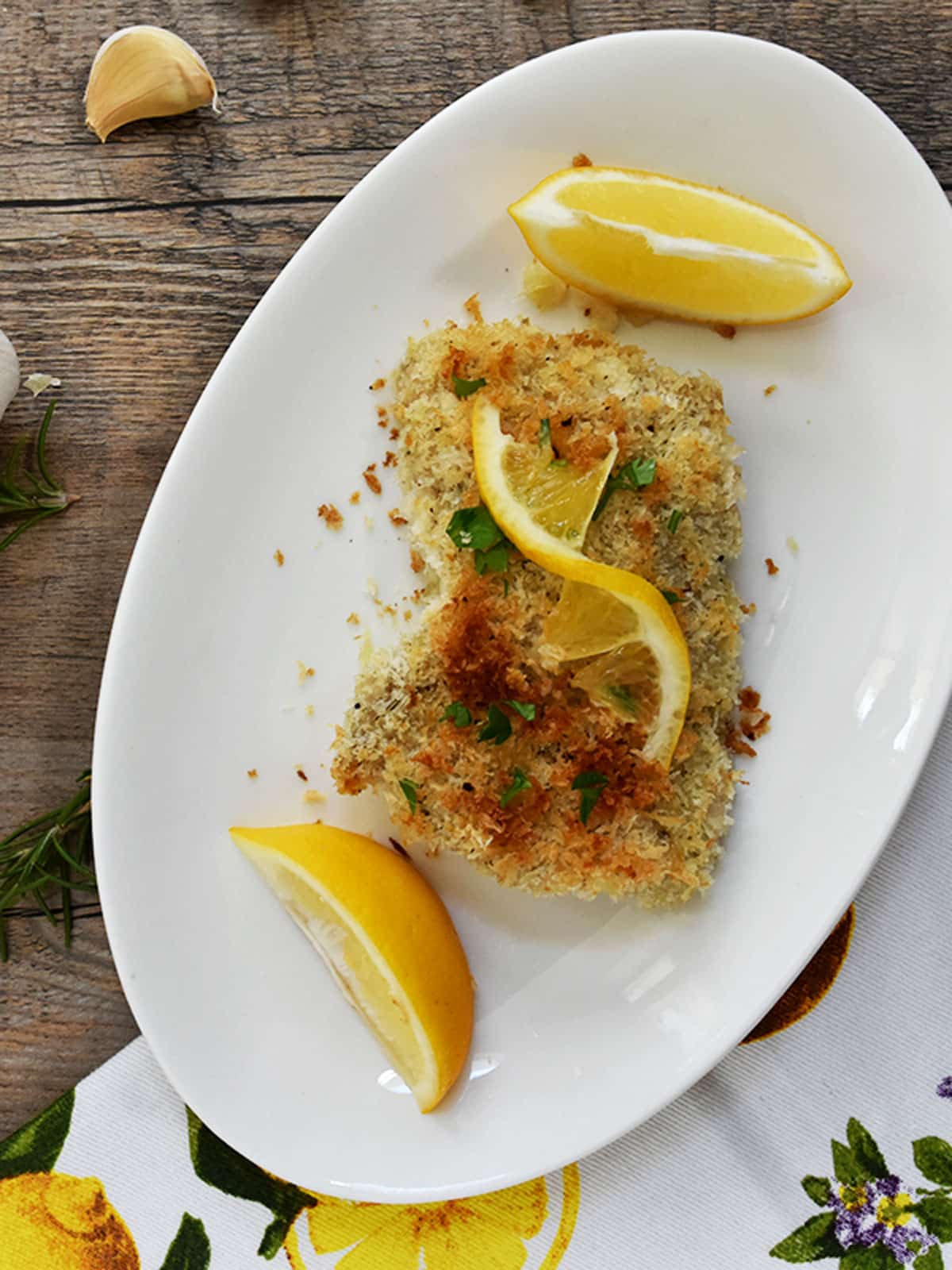 Breaded lemon chicken on a white plate with lemon quarters on either side.