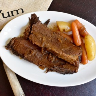 Instant Pot Brisket on white plate with carrots and potatoes and a YUM napkin and fork