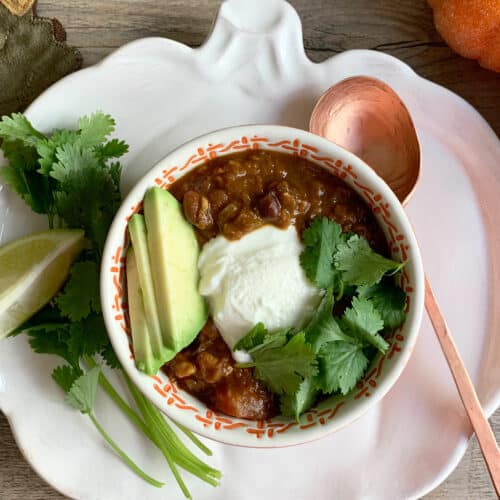 Instant Pot Red Lentil Chili in an orange bowl on a pumpkin plate with a copper spoon and pumpkins on the side.