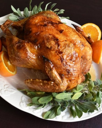 Whole Dry Brine Turkey Roasted on a white plate with fresh sage and oranges