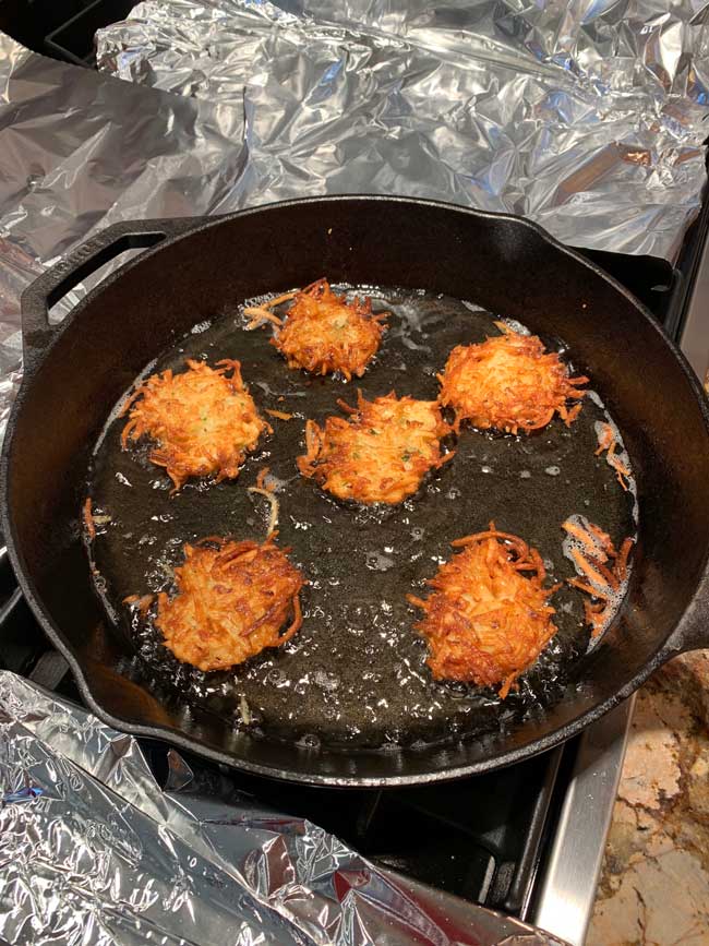 several latkes cooking in cast iron pan