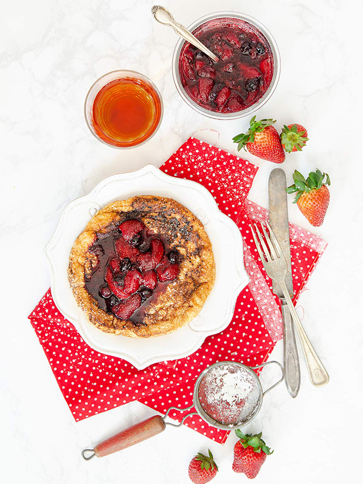 Matzo meal pancake or bubula with fruit compote on top on a white plate with tea and compote on the side.