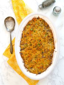 baked potato kugel in white casserole dish with yellow napkin and large serving spoon