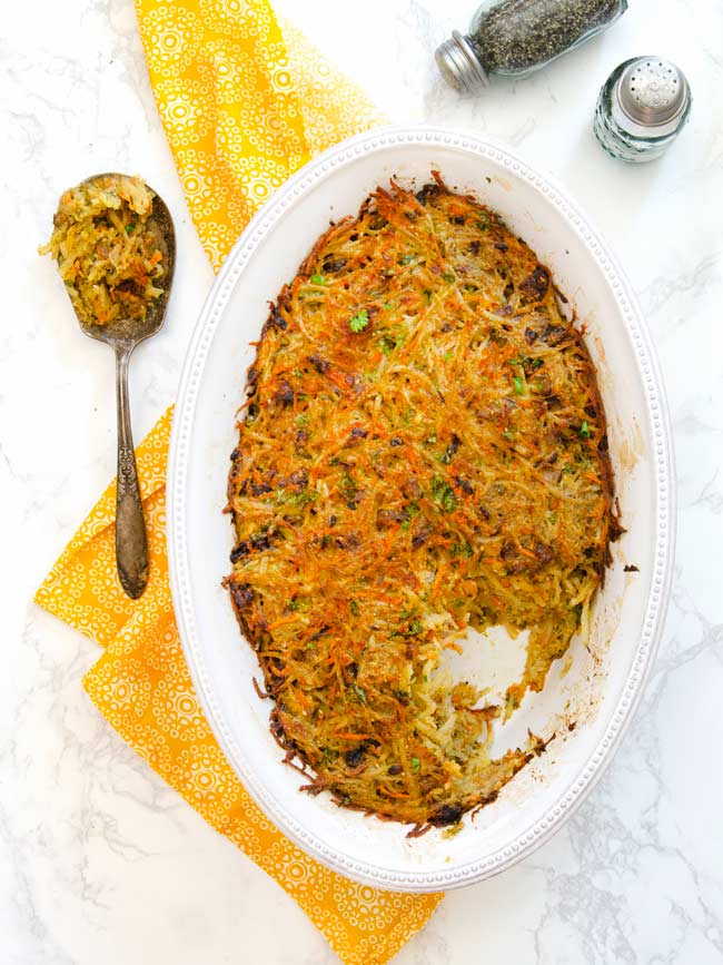 cooked crispy potato kugel in dish with serving spoon of kugel on the side