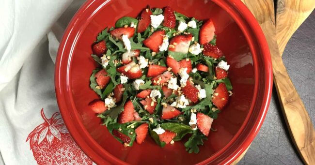 Strawberry spinach salad in a red bowl with wood servers on the side.