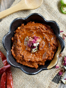 Rose harissa in a brown bowl with a wooden spoon on burlap cloth.