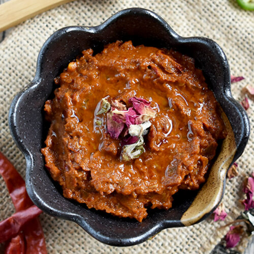 Rose harissa in a brown bowl with a wooden spoon on burlap cloth.