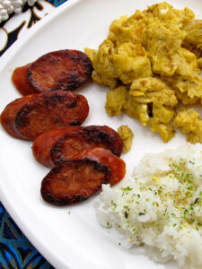 Portuguese sausage rice and eggs on a white plate with a Hawaiian napkin in the background.