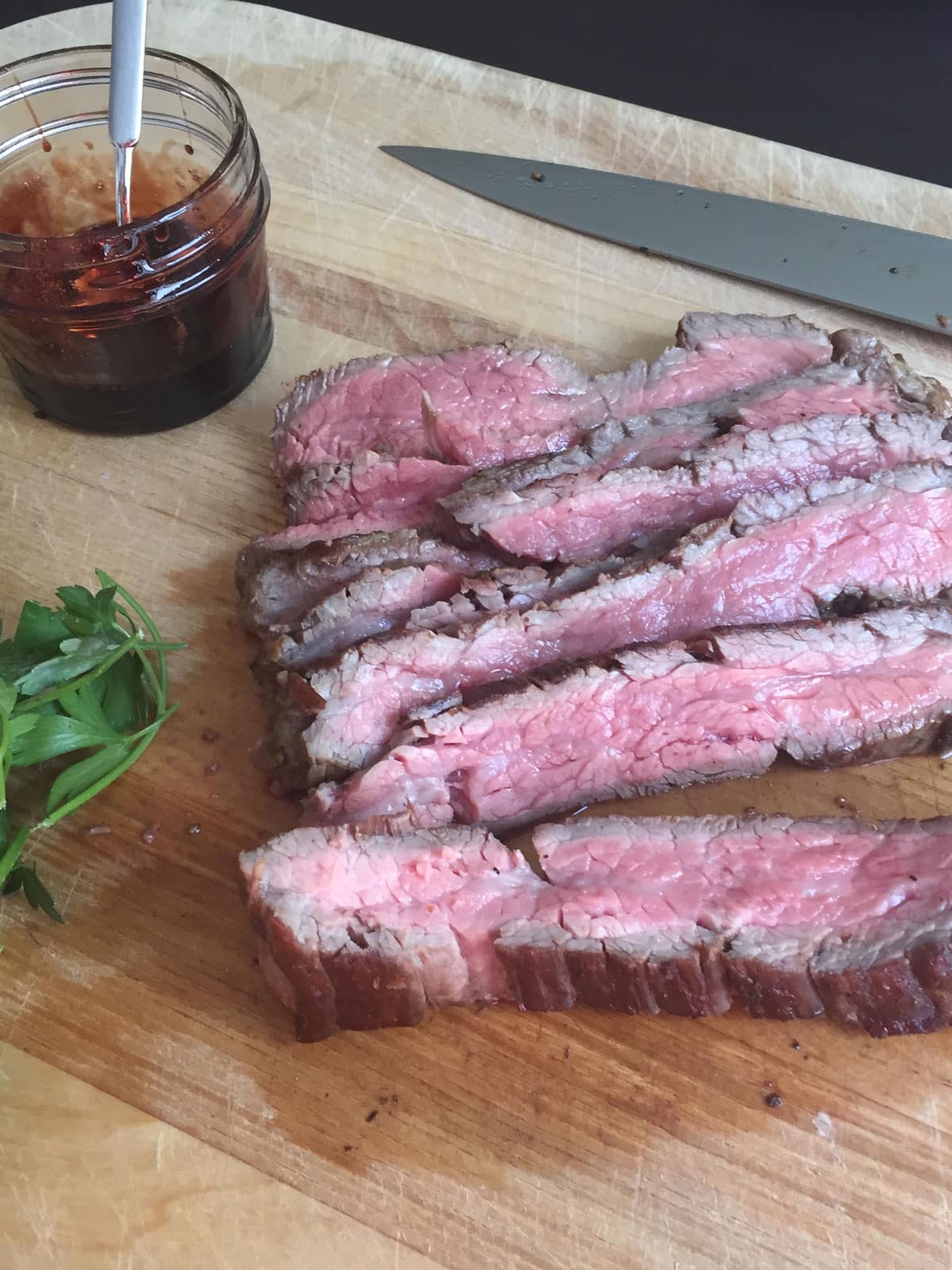 Flank steak on cutting board with pomegranate molasses on the side.