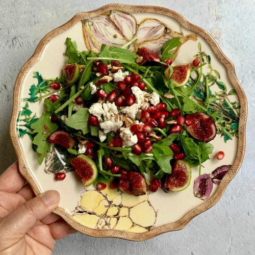 Arugula and Fig Salad on a plate with a hand holding the plate.