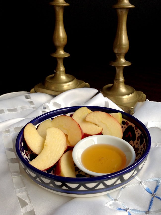 Apple slices and honey in a bowl with candlesticks in background.