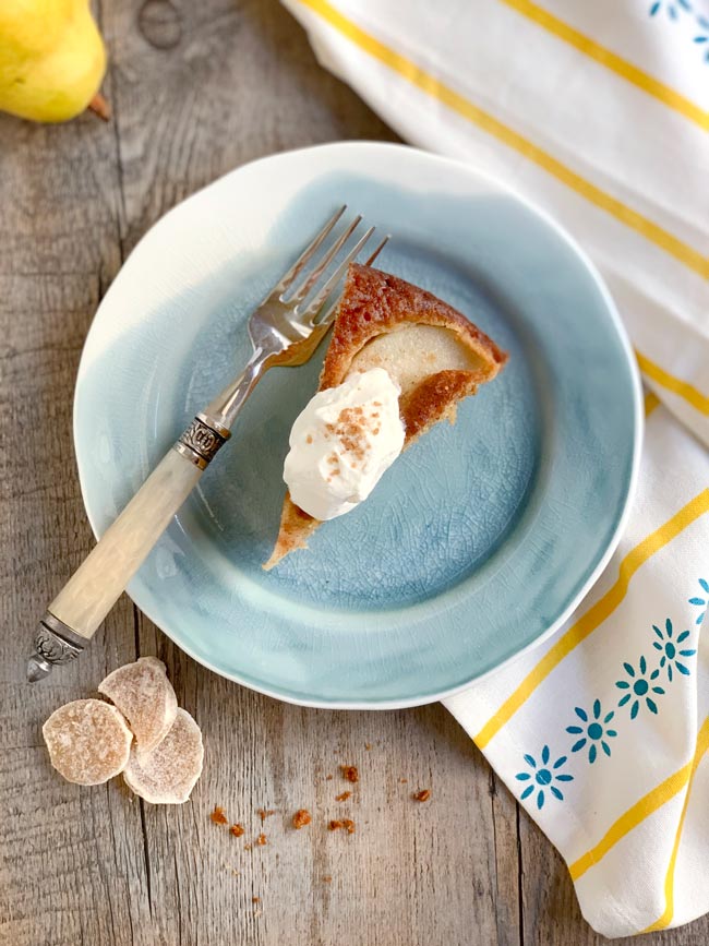 A slice of pear cake on blue plate with dollop of whipped cream.