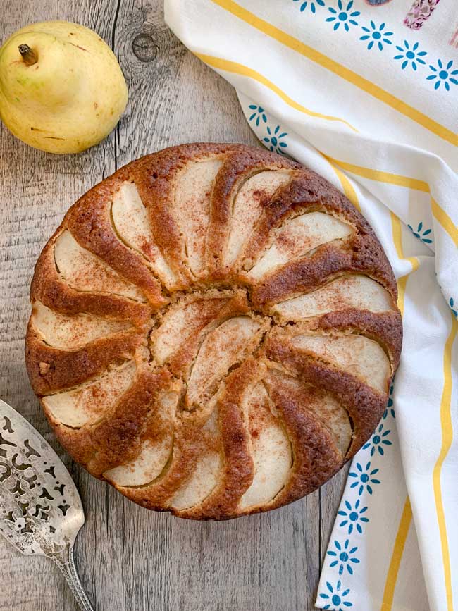 A whole pear cake with pear, cake server, striped napkin.