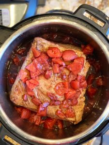 braising liquid with tomatoes poured over instant pot brisket with pomegranate molasses