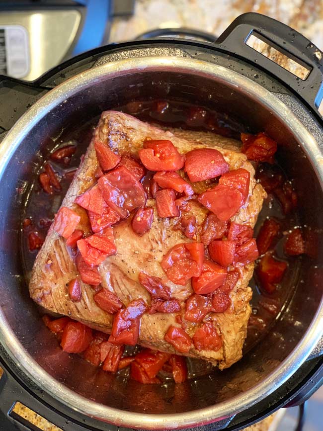 Braising liquid with tomatoes poured over instant pot brisket with pomegranate molasses.