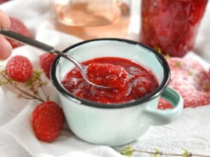 spoon of strawberry raspberry jam on white napkin with wine in background