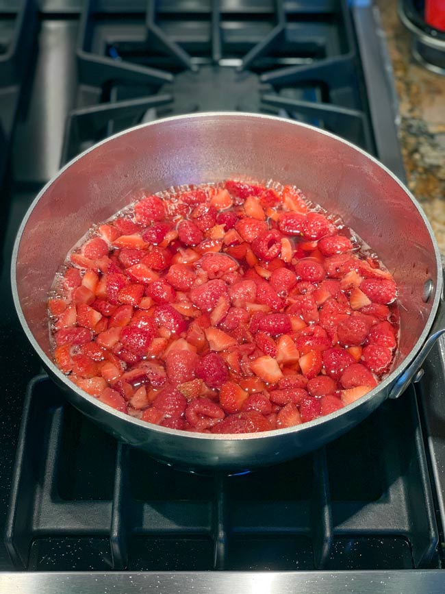 Strawberry and raspberry jam ingredients in a metal pot on stovetop boiling down.