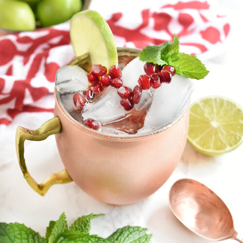 Copper mug with moscow mule in it topped with pomegranate arils and a lime.