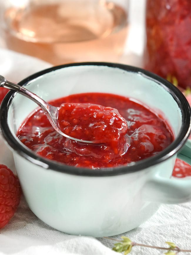 A spoon of Gregory's jam in blue bowl with rosé wine in the background.