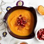 Roasted butternut squash soup in a purple bowl with a pomegranate napkin.