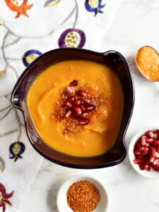 Roasted butternut squash soup in a purple bowl with a pomegranate napkin.
