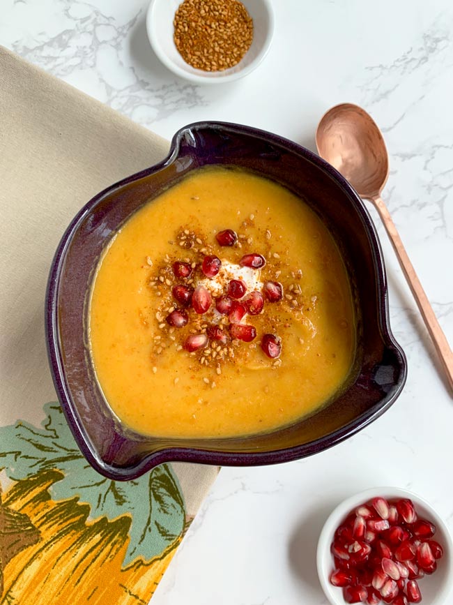 Butternut squash soup in bowl topped with yogurt and pomegranate and dukkah.
