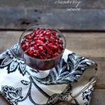 A bowl of cranberry pomegranate sauce on a white and black leaved napkin with a wood background.