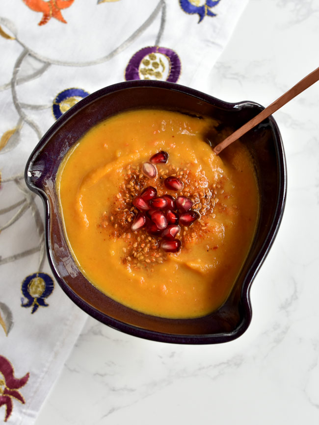Squash soup in purple bowl with copper spoon.