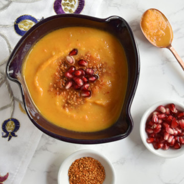 soup in purple bowl with copper spoon and dukkah and arils