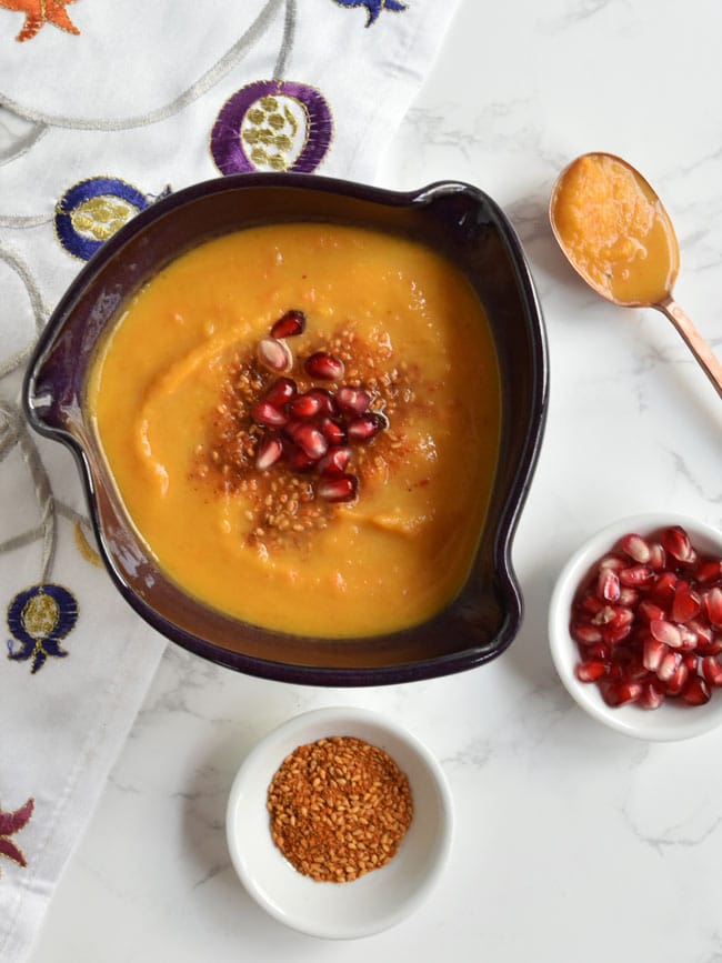 Soup in purple bowl with copper spoon and dukkah and arils.