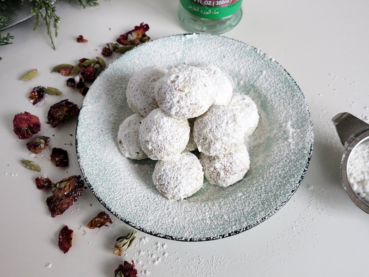 Pistachio snowballs on a teal plate with sifter and dried rose petals.